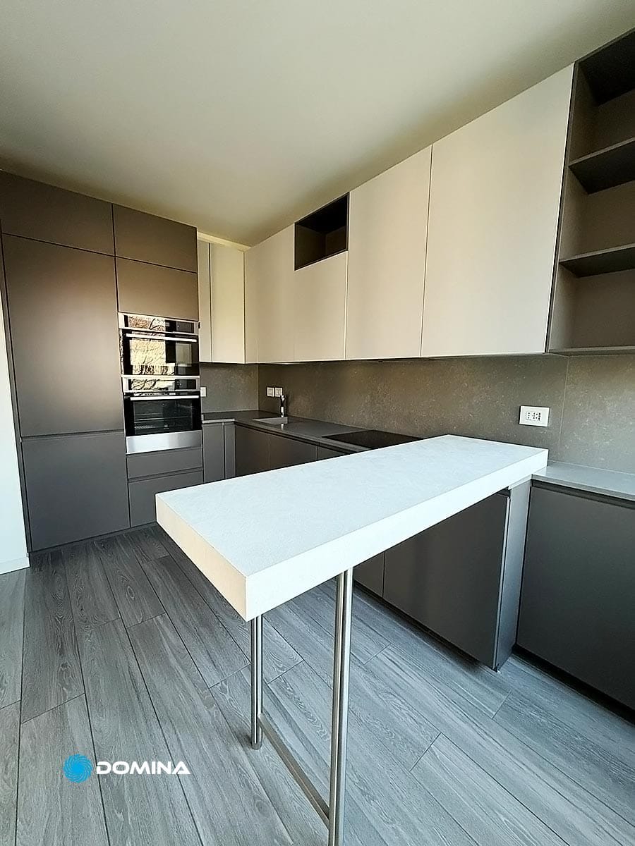 079-pulizie-appartamenti-city-life-milano-domina-pulizie-21022025 Cucina moderna con mobili grigi, forni incorporati, un piano di lavoro bianco alto e pavimento in legno. Design minimalista con linee pulite, perfetto per chi apprezza le pulizie di lusso City Life Milano.