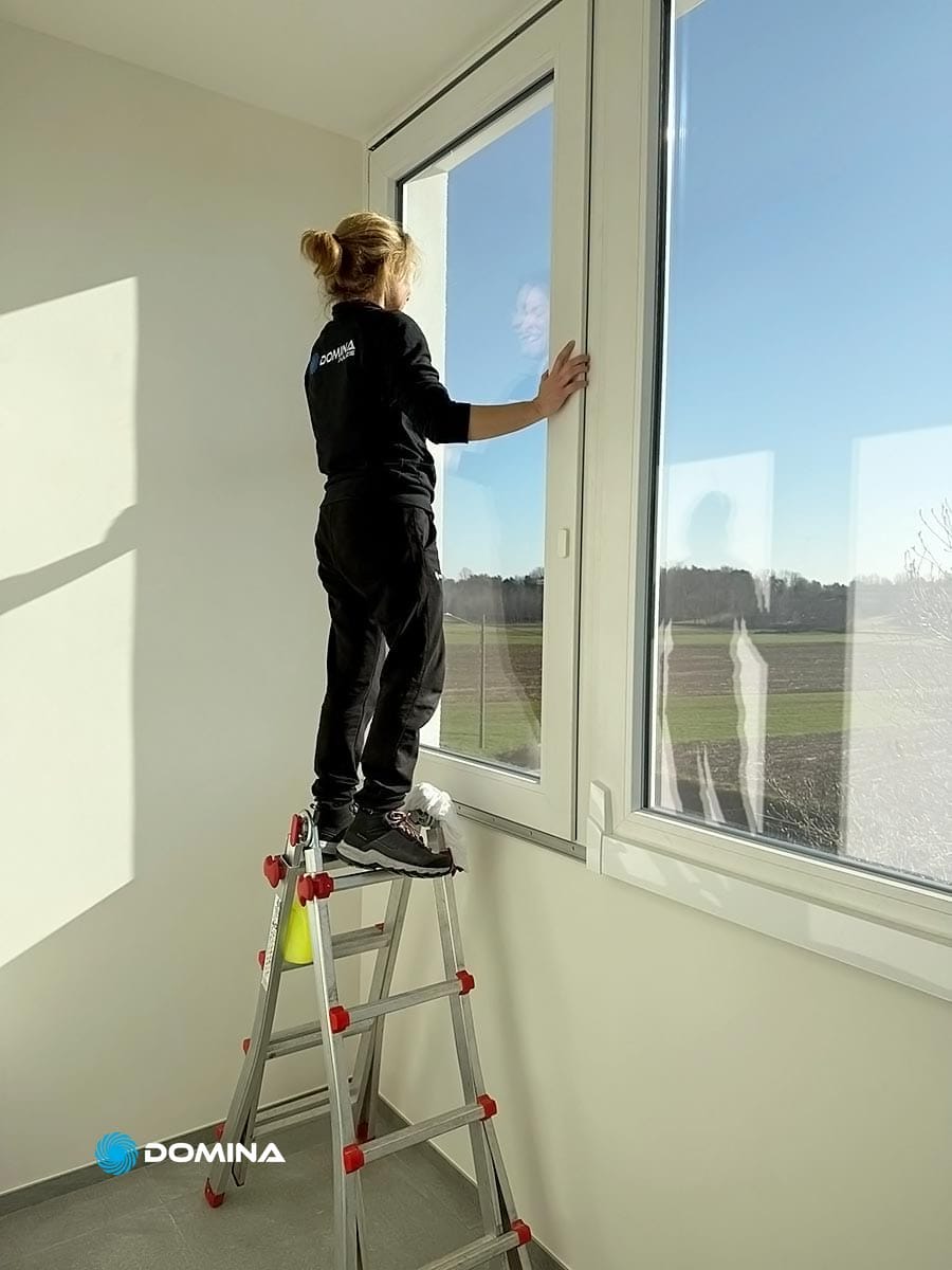 088-impresa-pulizie-trezzano-sul-naviglio-milano-domina-pulizie-21022025 Una persona è in piedi su una scala a pioli e mostra la sua professionalità mentre pulisce una grande finestra in una stanza luminosa che si affaccia sui campi di Trezzano sul Naviglio.