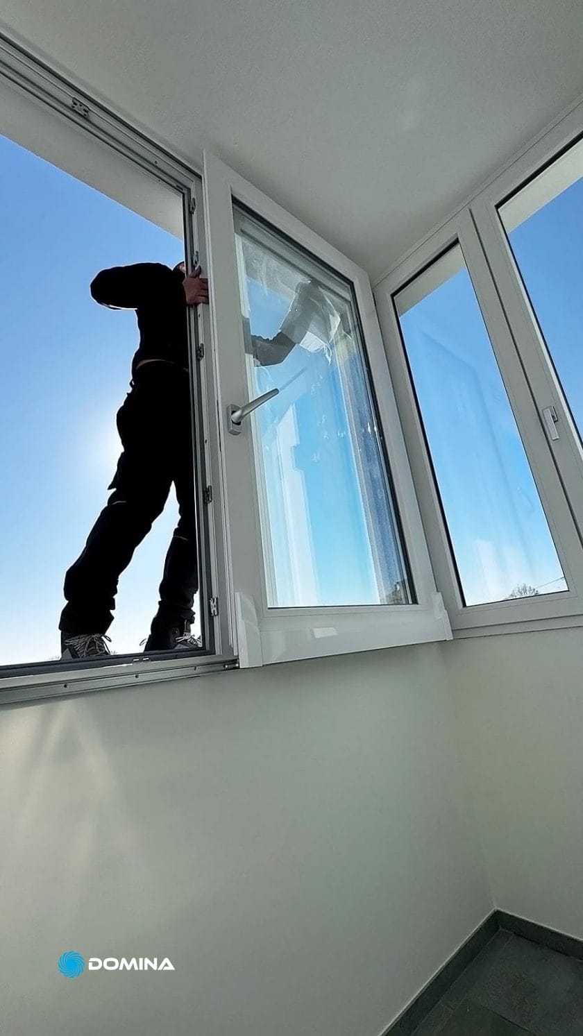 Una persona è in piedi sul davanzale di una finestra, incorniciata in modo impeccabile dalla finestra e con un cielo azzurro limpido sullo sfondo, come se fosse pronta a sorvegliare una Pulizia Casa Fine Locazione a Busto Arsizio.