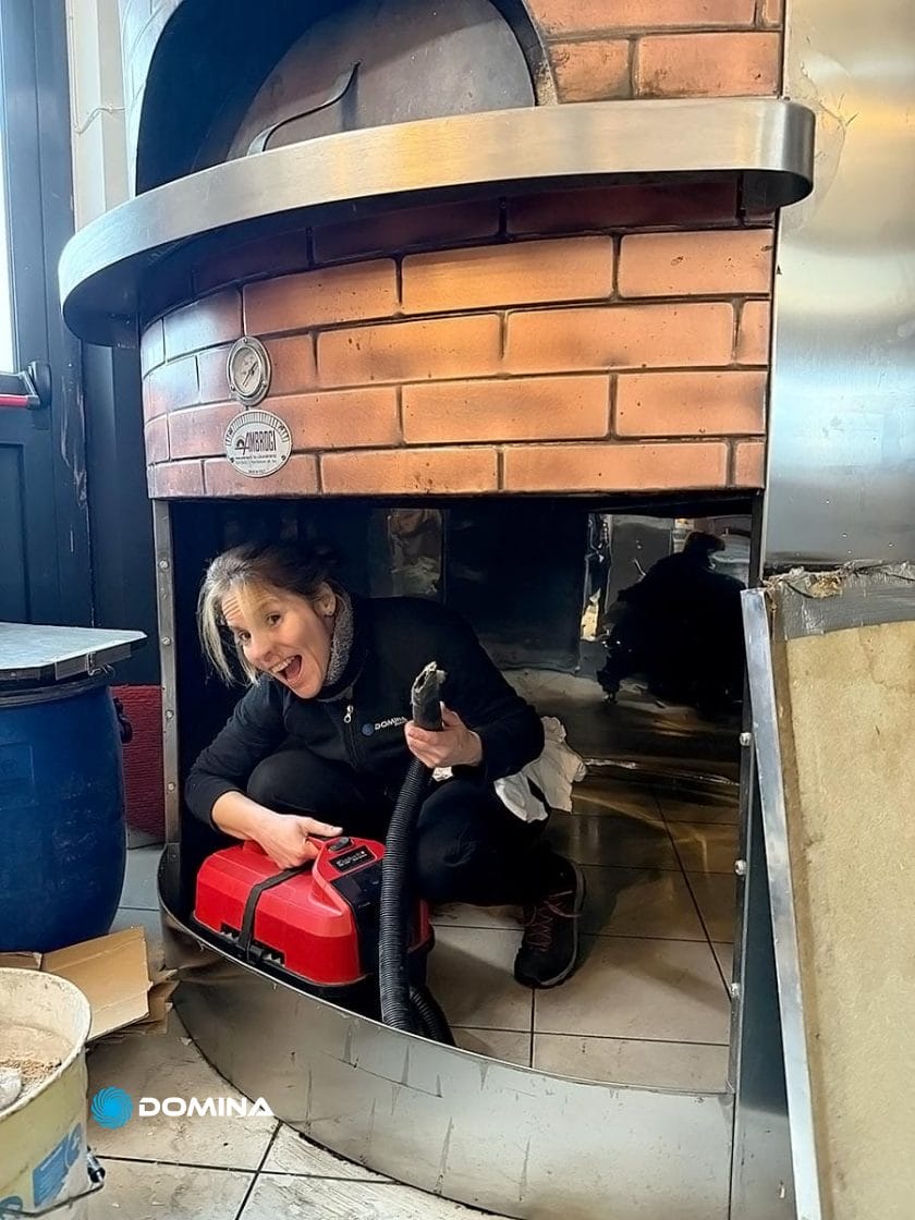 Un addetto dell'Impresa di Pulizie è accovacciato all'interno di un forno di mattoni, tiene in mano un aspirapolvere e sorride alla telecamera.