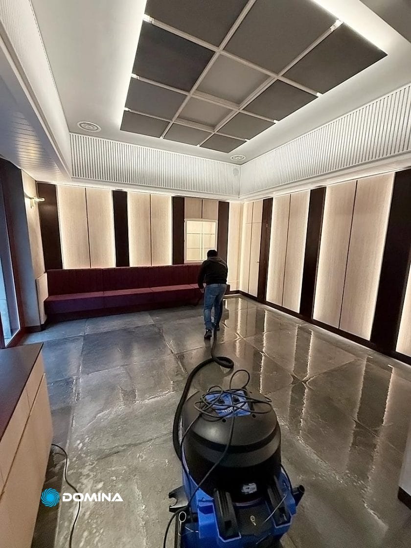 Un addetto di un'impresa di pulizie per ristoranti di Milano pulisce con cura una stanza spaziosa e moderna con un pavimento in pietra lucidata, manovrando con perizia la macchina per la pulizia per far sì che ogni angolo brilli.