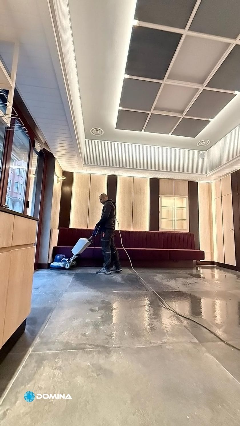 Una persona aziona una macchina per la pulizia dei pavimenti in una stanza moderna e spaziosa, con pannelli in legno e luci al soffitto, garantendo gli standard di pulizia ottimali attesi dall'impresa di pulizie per ristoranti Milano.