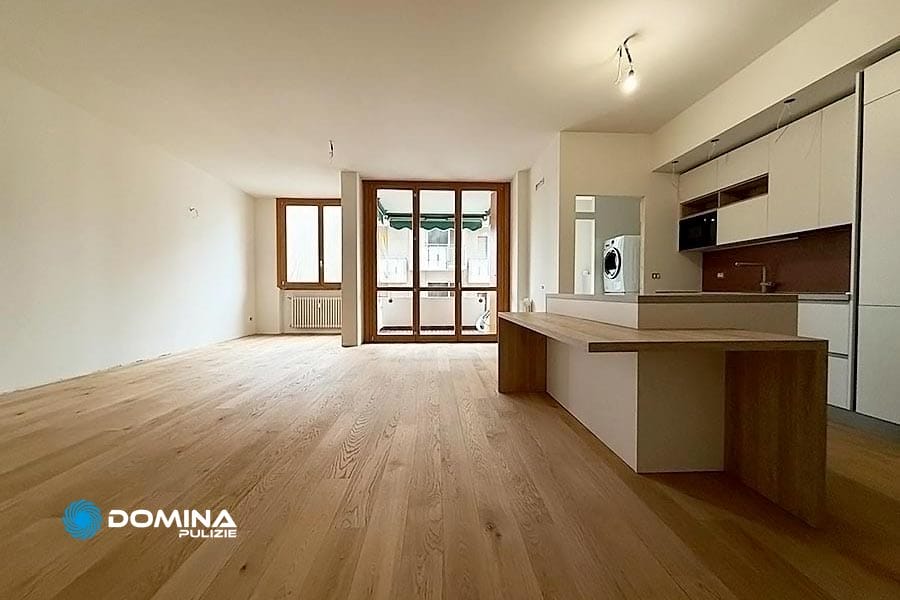 Ampia stanza vuota con pavimenti in legno, una moderna zona cucina perfetta per le pulizie di casa, primo ingresso e grandi finestre che conducono a un balcone con vista sulla bellezza di Milano.