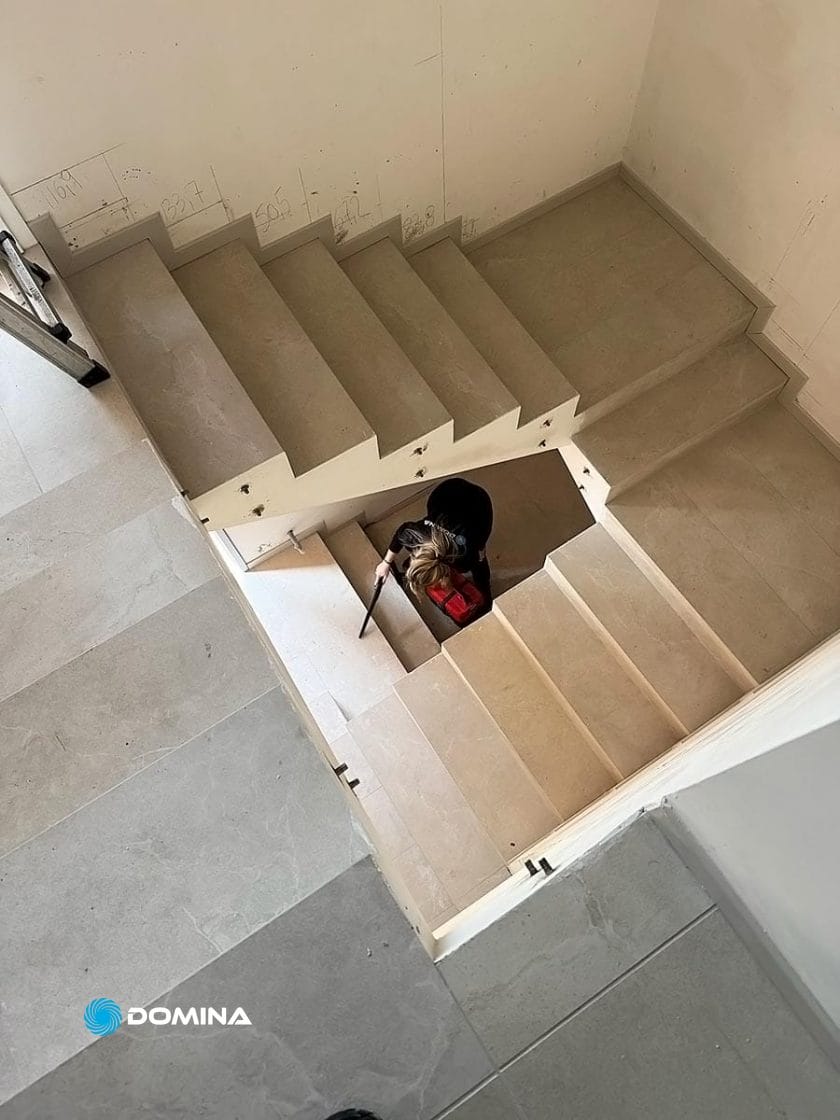 Una persona con uno zaino rosso scende una scala interna incompiuta a Nova Milanese, vista dall'alto. Pareti e scale non sono tinteggiate e sono visibili i segni dei lavori, in attesa del tocco di un'impresa di pulizie Domina.