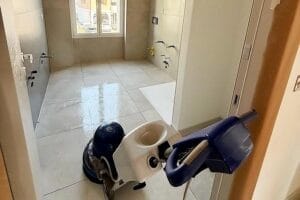 Una macchina lavapavimenti Domina è posizionata all'ingresso di un bagno piastrellato e non arredato o di una cucina con finestra sul retro, a sottolineare la professionalità dell'impresa di pulizie Nova Milanese.