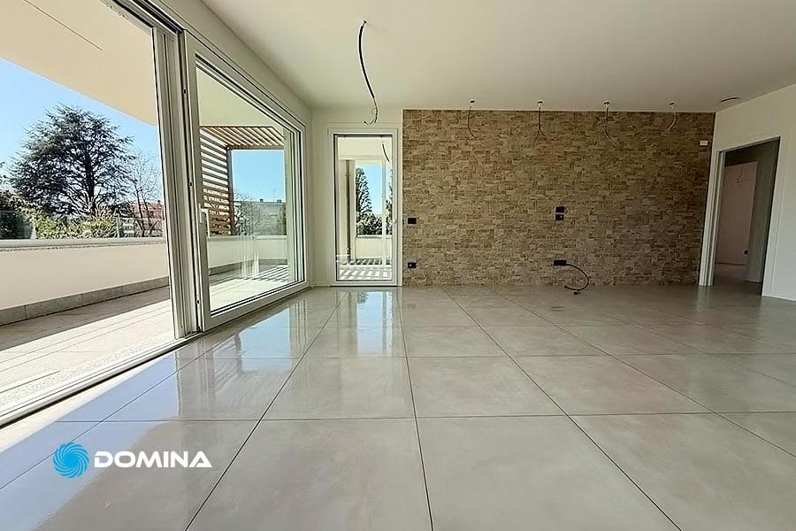 Soggiorno moderno non arredato in una casa nuova, con ampio pavimento in piastrelle, porte scorrevoli in vetro a tutta altezza, una parete con elementi in pietra e accesso a un patio esterno a Rozzano. Pulizie Fine Cantiere consigliato per finiture impeccabili.