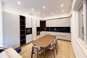 Cucina moderna con mobili chiari, paraschizzi nero, tavolo da pranzo in legno e sei sedie su pavimento in legno chiaro: ideale per Pulizie Primo Ingresso a Tradate per garantire che ogni dettaglio brilli fin dal primo giorno.