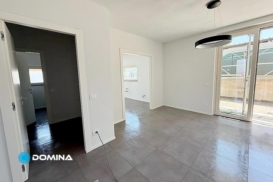 Stanza moderna, luminosa e vuota, con pavimenti piastrellati, pareti bianche, grande finestra e lampadario nero appeso, perfettamente pulita dopo le pulizie post cantiere a Cadrezzate.