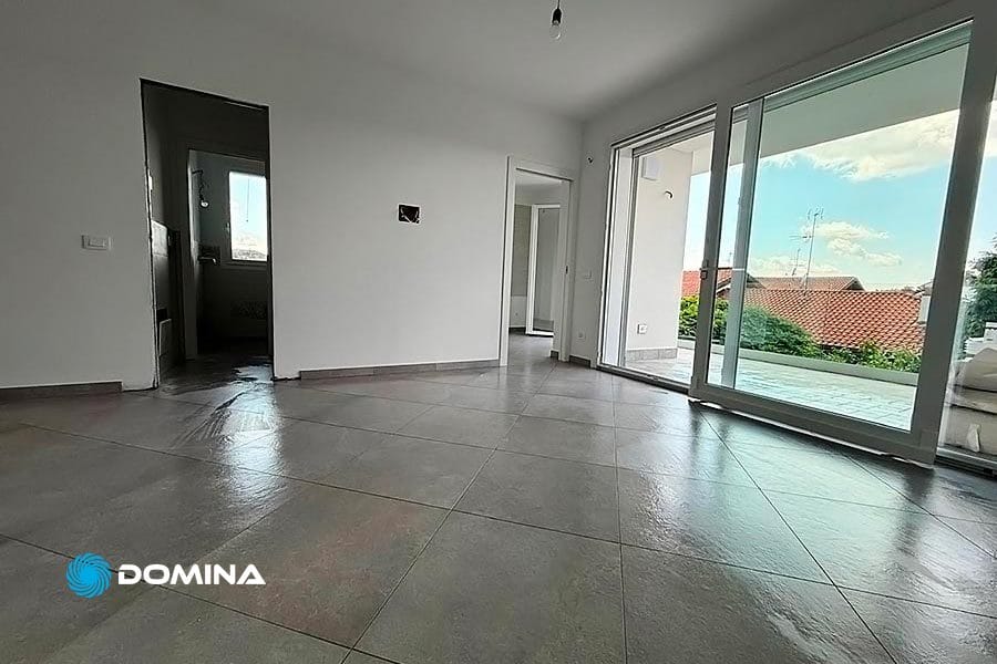 Stanza luminosa e vuota con ampio pavimento piastrellato, porte aperte e finestre con vista sui tetti e sul cielo, perfettamente pulita dopo le pulizie fine cantiere a Sesto Calende.
