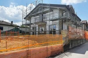 Una casa in fase di ristrutturazione con impalcature e reti di sicurezza arancioni attorno al cantiere, pronta per Pulizie Fine Cantiere Villa Travedona Monate.