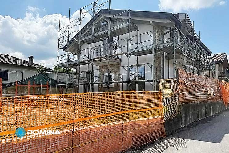 Una casa in fase di ristrutturazione con impalcature e reti di sicurezza arancioni attorno al cantiere, pronta per Pulizie Fine Cantiere Villa Travedona Monate.