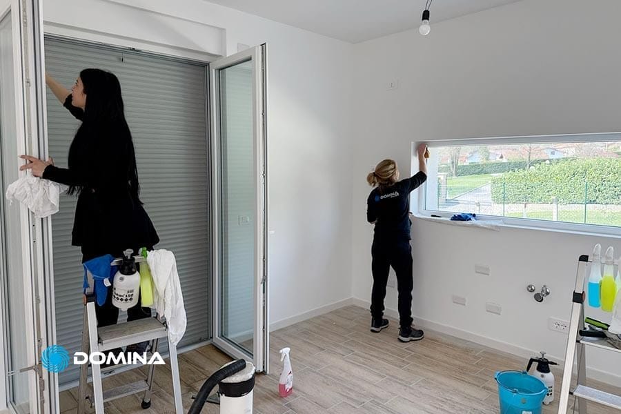 Due donne puliscono le finestre in una stanza luminosa e moderna con prodotti per la pulizia sul pavimento, specializzate in Pulizie Post Cantiere Como.