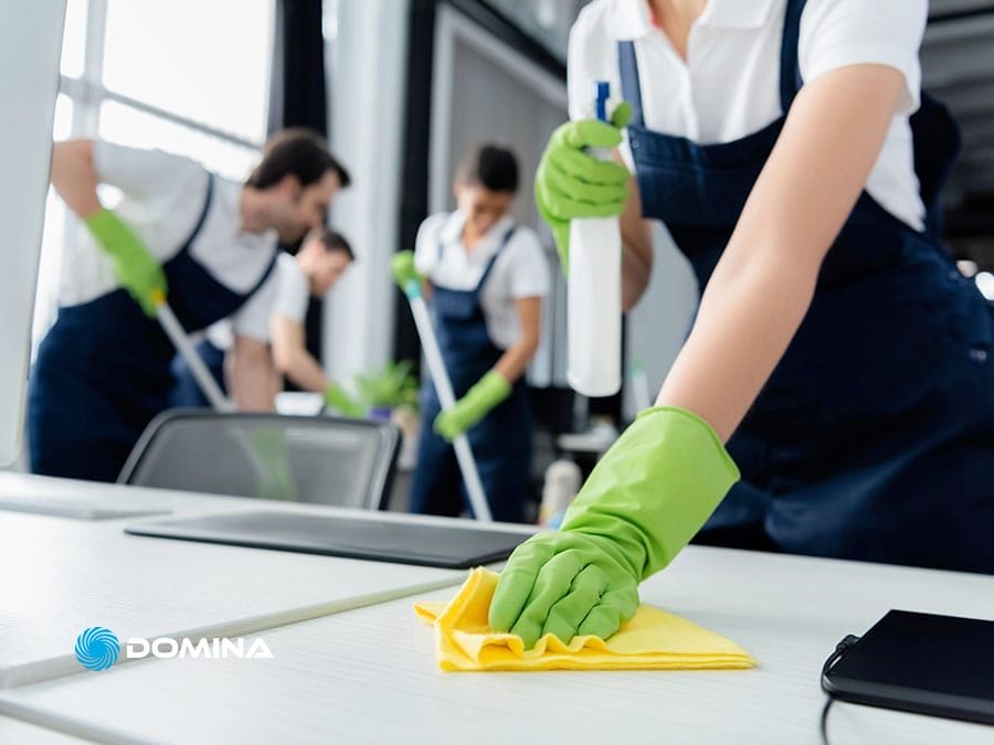 pulizie-uffici-2 Persone in uniforme e guanti verdi puliscono le scrivanie in un ufficio con panni e flaconi spray, assicurando una pulizia accurata e un ambiente di lavoro impeccabile e professionale.