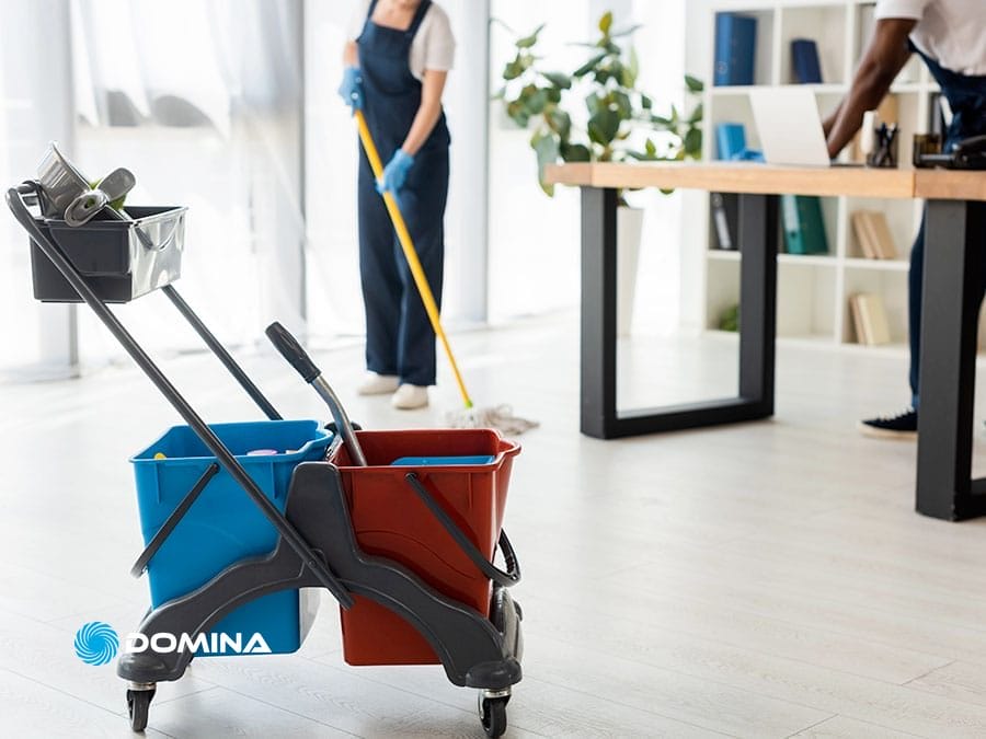 pulizie-uffici-3 Carrello per prodotti per la pulizia e due persone che puliscono un ufficio luminoso con uno straccio e spolverano una scrivania, offrendo Pulizie Uffici a Garbagnate Milanese e nei Comuni limitrofi per spazi di lavoro impeccabili e accoglienti.