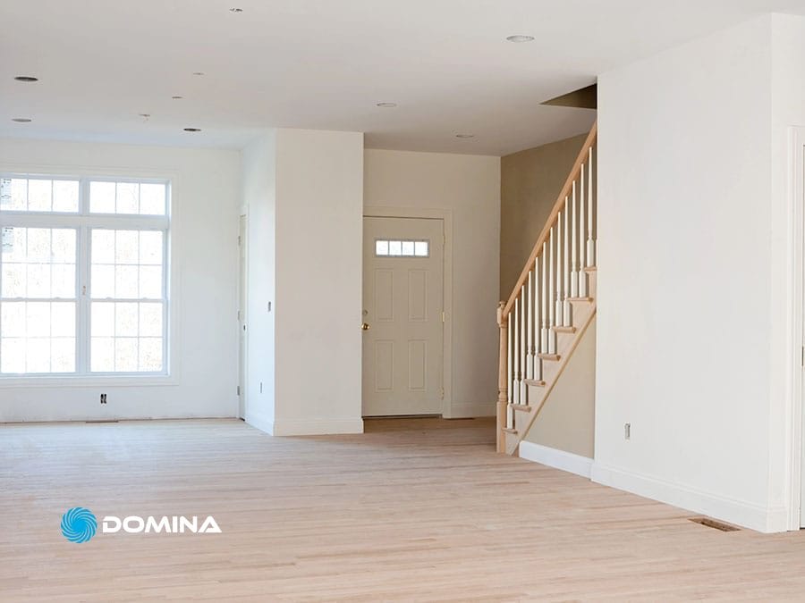 servizi-imbiancatura-2 Stanza vuota e non arredata con pavimenti in legno chiaro e pareti bianche che mettono in mostra i risultati dell'imbiancatura professionale, una scala, una grande finestra e una porta d'ingresso.