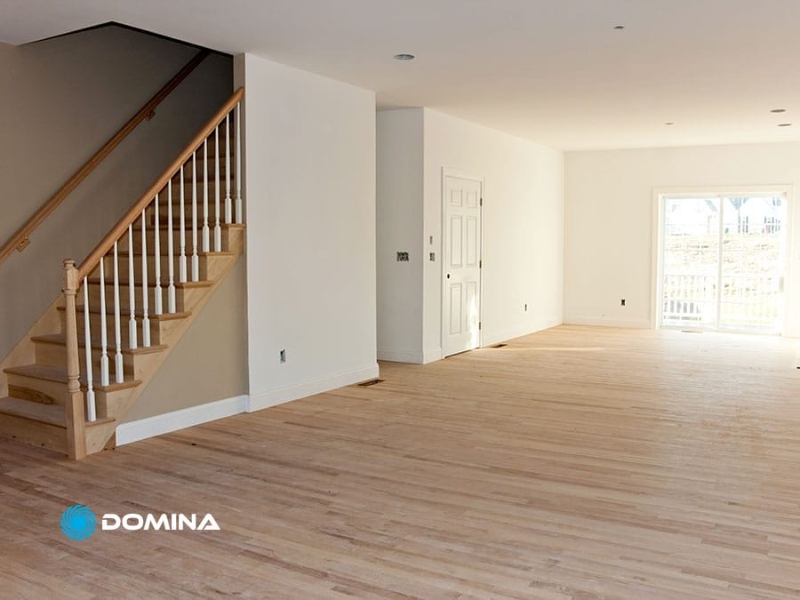 servizi-imbiancatura-4 Stanza non arredata con pavimenti in legno chiaro, scala e pareti bianche, imbiancatura professionale. Una porta conduce a un patio soleggiato, che mette in risalto la qualità dei servizi di imbiancatura offerti da un imbianchino esperto.