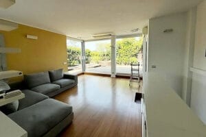 Soggiorno luminoso con divano grigio, pavimenti in legno, ampie finestre e vista su un patio soleggiato e sul giardino, perfettamente curato grazie a Pulizie Appartamenti Legnano.