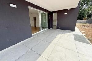 Ampio patio piastrellato con porte scorrevoli in vetro, pareti scure e vista su uno spazio interno moderno, perfettamente rinnovato dopo le pulizie post cantiere di Tradate.