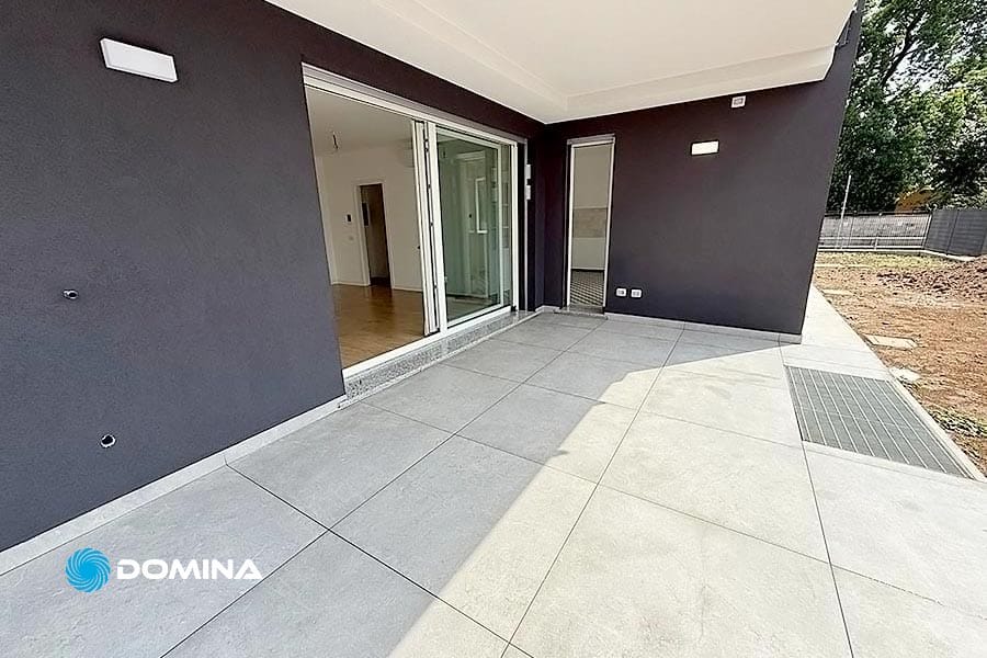 Ampio patio piastrellato con porte scorrevoli in vetro, pareti scure e vista su uno spazio interno moderno, perfettamente rinnovato dopo le pulizie post cantiere di Tradate.