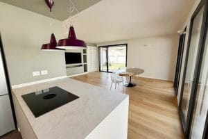 Moderna cucina e zona giorno a pianta aperta con pavimenti in legno, isola e ampie finestre che lasciano entrare la luce naturale, senza macchie grazie alle pulizie post cantiere Vedano Olona.