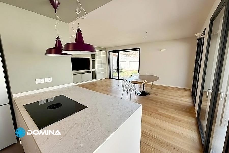 Moderna cucina e zona giorno a pianta aperta con pavimenti in legno, isola e ampie finestre che lasciano entrare la luce naturale, senza macchie grazie alle pulizie post cantiere Vedano Olona.