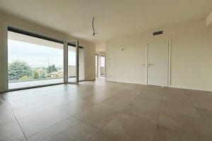 Spaziosa stanza vuota con ampio pavimento in piastrelle, pareti bianche e porte scorrevoli in vetro che si aprono su un balcone: ideale per pulizie appartamenti Legnano o per chi cerca pulizie straordinarie legnano prima di trasferirsi.