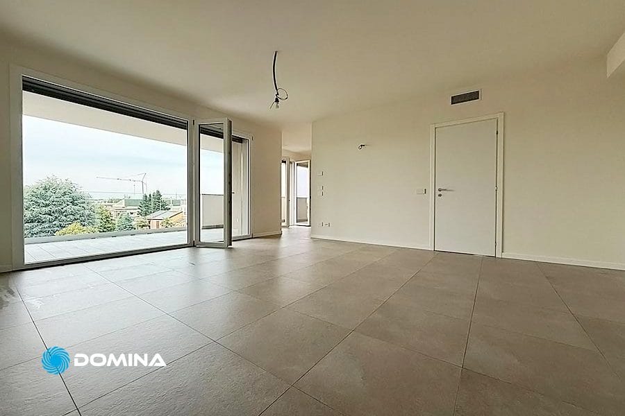 Spaziosa stanza vuota con ampio pavimento in piastrelle, pareti bianche e porte scorrevoli in vetro che si aprono su un balcone: ideale per pulizie appartamenti Legnano o per chi cerca pulizie straordinarie legnano prima di trasferirsi.