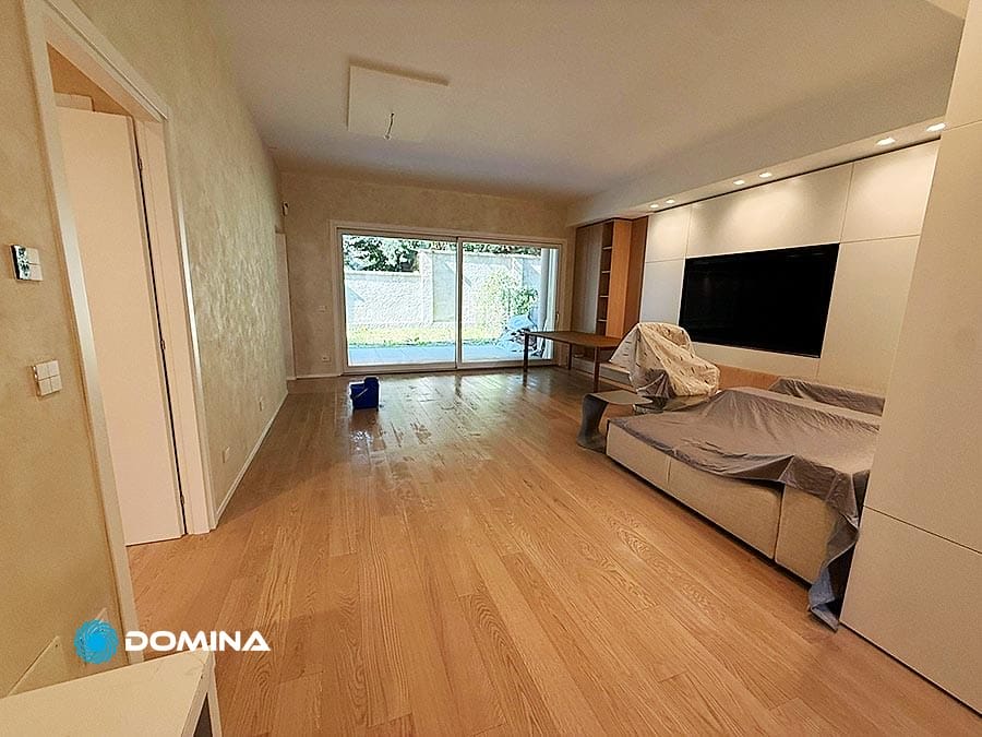Ampio soggiorno con pavimento in legno, grande finestra, divano, TV e mobili sparsi coperti da lenzuola - ideale per Pulizie Post Cantiere dopo una ristrutturazione in City Life Milano.