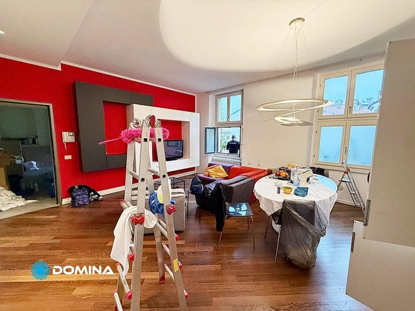 Un soggiorno moderno con pareti bianche e rosse, pavimenti in legno, un divano grigio e materiale per le pulizie fa pensare a un servizio di pulizia appartamenti Porta Garibaldi Milano in corso, perfetto per chi cerca uno spazio impeccabilmente pulito.