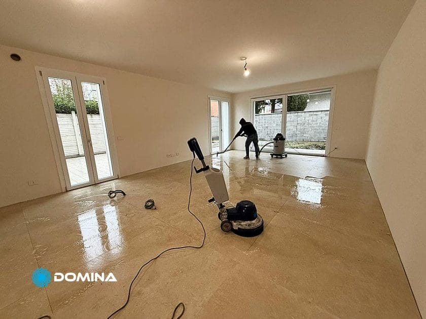 Una persona usa l'attrezzatura per la pulizia per lucidare il pavimento in un'ampia stanza vuota con piastrelle beige e pareti bianche a Rho, che mostra Casa Pronta pulizie fine cantiere con luce naturale che filtra dalle grandi finestre.