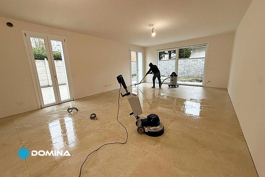 Due persone stanno pulendo il pavimento in piastrelle di una stanza vuota e non arredata a Rho, piena di luce naturale. Utilizzando macchine lavapavimenti, eseguono Pulizie Fine Cantiere per garantire che lo spazio sia immacolato e pronto per Casa Pronta.